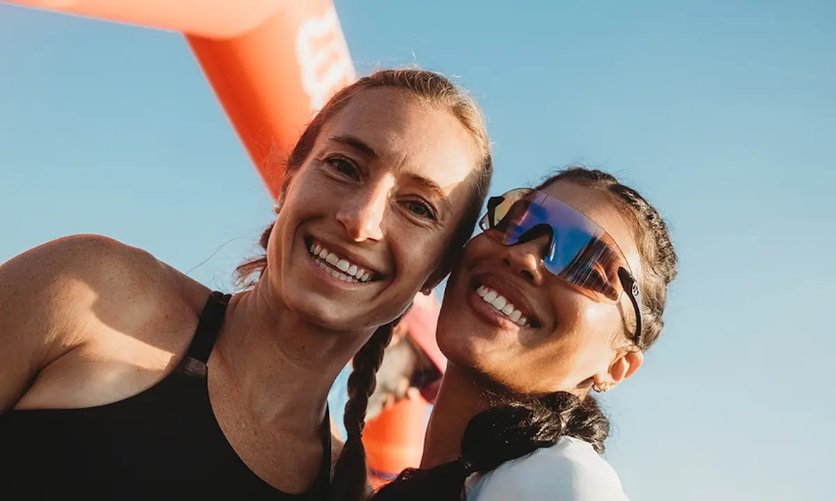 Two smiling women in athletic gear posing beneath a red event arch