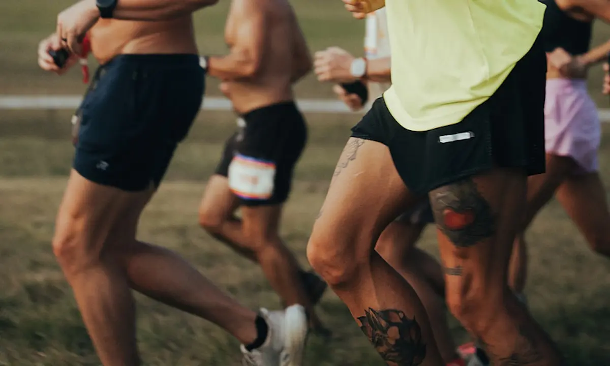 Group of runners mid-stride, focus on tattooed legs and running shorts