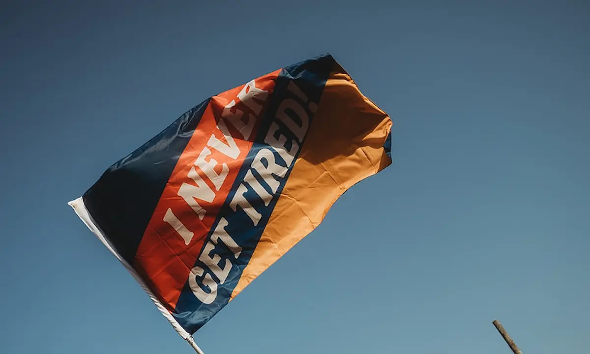 Waving flag reading 'I NEVER GET TIRED' against clear blue sky