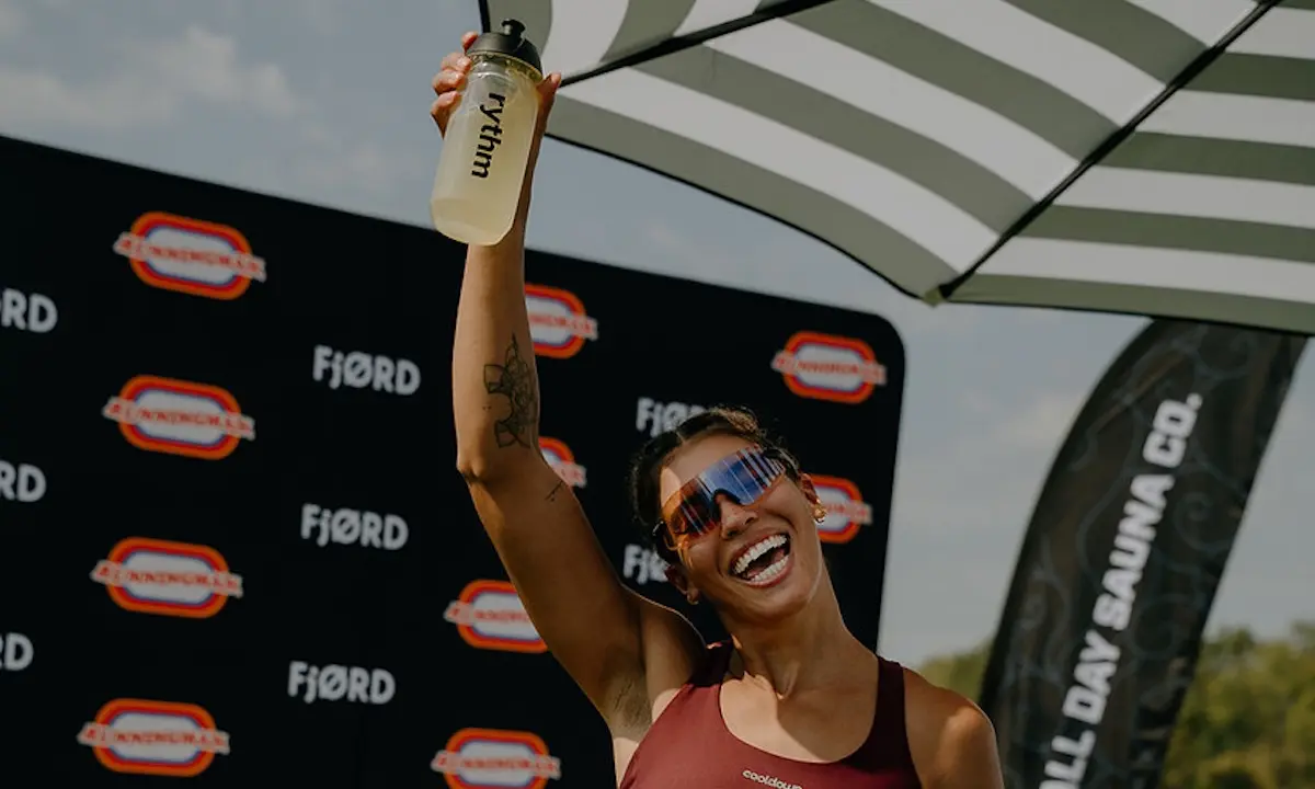 Smiling woman raising a water bottle in front of a FJØRD event backdrop
