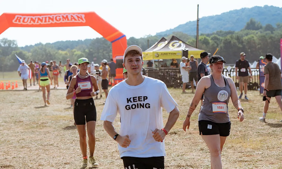 Runners passing under orange RUNNINGMAN arch; man in 'KEEP GOING' shirt