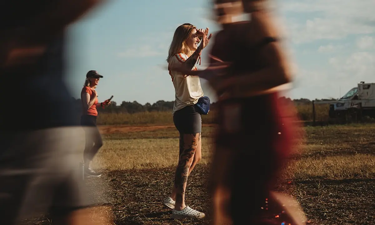 Woman shielding her eyes outdoors at a field event as others pass by