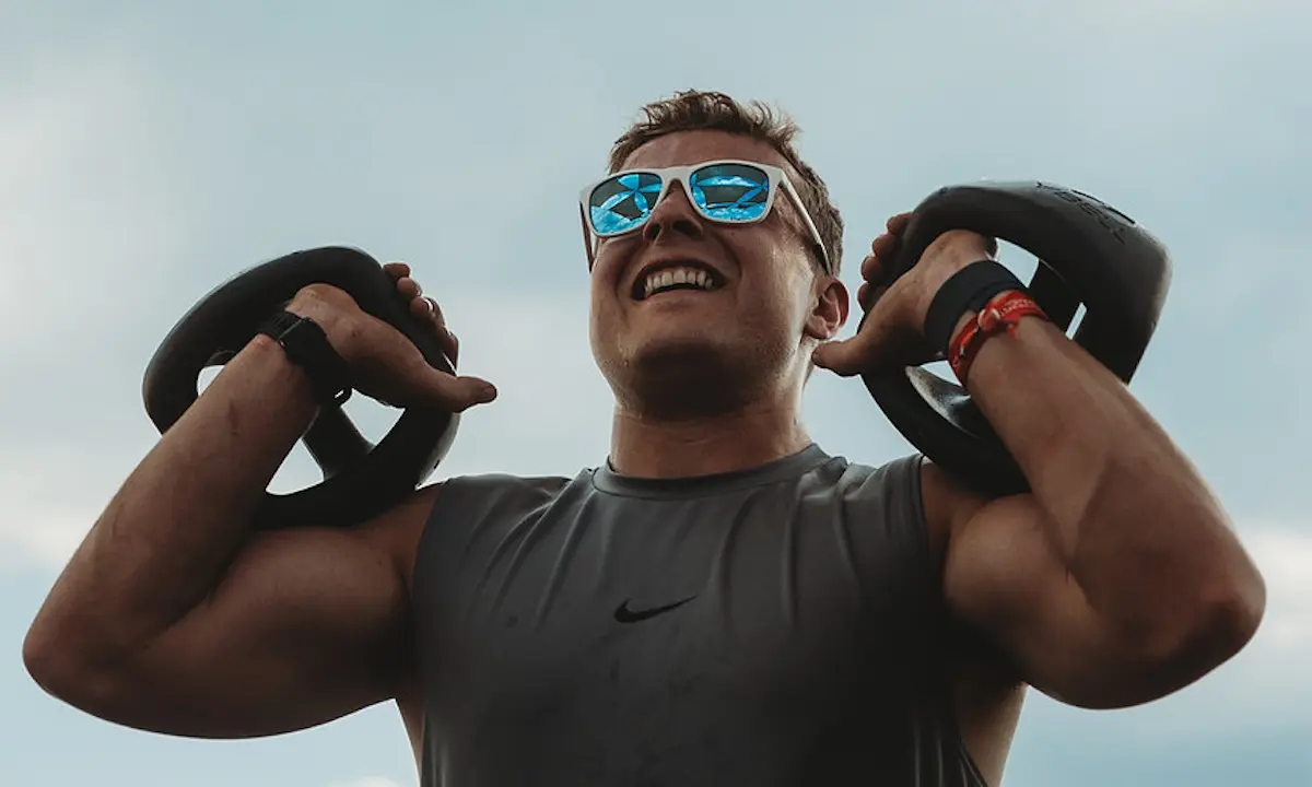 Smiling man lifting kettlebells to shoulders during outdoor workout